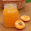 Jar of apricot jam and an apricot cut in half on a table.