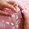 A person crocheting a pink baby blanket.
