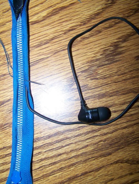 close up of zippered ear bud case on a table with one earbud laying next to it