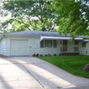 Looking up the driveway to older home. It has a one car attached garage and an aluminum awning over door and front windows.