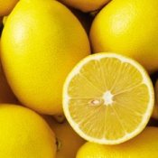 A half lemon sitting ontop of a pile of whole lemons.