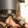 Repairing a Garbage Disposal (Disposer), Man's hands holding a power screwdriver to a garbage disposal.