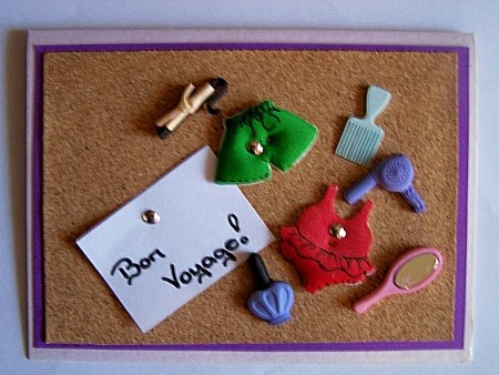 Finished Bon Voyage Card with foam swimsuits, brush, curling iron attached to cork board with brads.