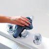 Woman's hand holding blue cloth cleaning the tub spout.