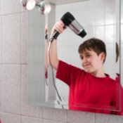 Cleaning Bathroom Mirrors, Reflection in a mirror of boy drying his hair with a blow dryer.