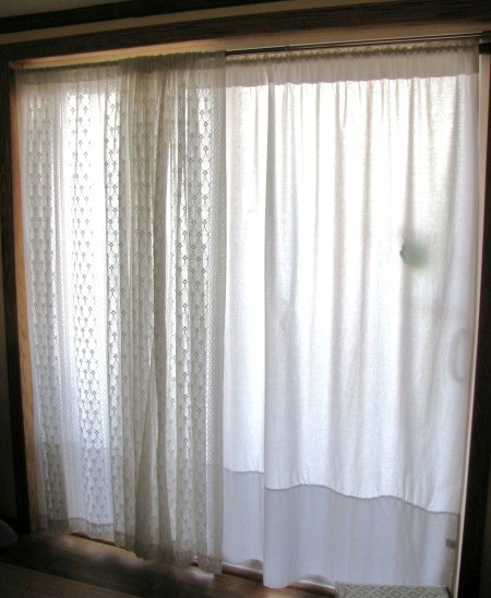 Sliding glass doors with white twin sheets as curtains behind lace curtains.