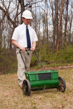 Man in tie and hard hat pushing a lawn mower