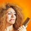Beautiful woman with frizzy hair looking at her comb, with a pained expression