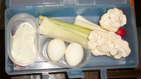 Lunch box with a Good Value container full of dip, one full of eggs, and celery and cauliflower loose in the box