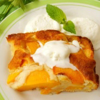 Square of peach cobbler on a plate with whipped cream on the side.