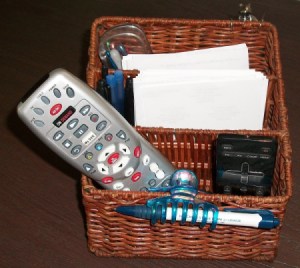 A basket with TV remotes, pens, paper and other small useful tools.