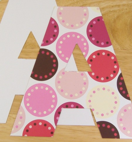 Two upper case letter A's cut out laying one on top of the other. bottom one has white side face p top on hase colorful pink and bron dots on it