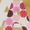 Two upper case letter A's cut out laying one on top of the other. bottom one has white side face p top on hase colorful pink and bron dots on it