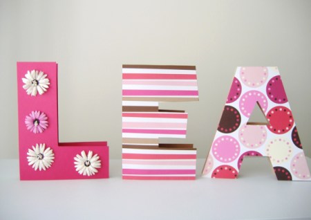 The name Lea completed as three dimensional blocks covered in patterened paper, the L has a line silk daisies going from top to bottom on th front