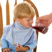 Man's hand helping a young boy drink his juice.