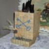 chick feeder covered in old paper with cut out of skeleton keys crossing each other, a few strands of raffia wrap the box near the bottom wiht a feather and a pewter and rhinestone button on it, the feeder is filled with pens