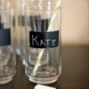 Tall Glasses with black stripe of chalkboard painted on them. The glass centered inthe image has Kate written on it, a yellow striped straw in the glass and a piece of chalk laying in front.