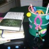 Teal bucket with hair ties and beads attached on a desk next to some books