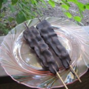 Two strips of bacon threaded on skewer and coated in chocolate displayed on a plate