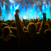 A large crowd in front of a nighttime concert with bright stage lights.