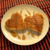Two heart shaped pancakse on a plate with syrup drizzled over them.