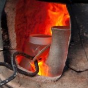 View of pottery kiln with tongs adjusting a piece.