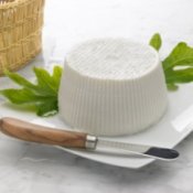 Ricotta cheese on fig leaves on white plate, with cheese knife.