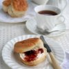 Scone on a plate with tea cup and saucer off to upper right.