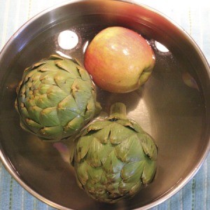 Bowl containing two artichokes and an apple in veggie wash.