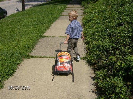 Small boy pulling a loaded sledge or similar wheeless conveyance down the sidewalk.