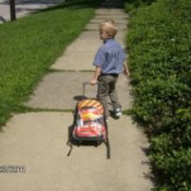 Small boy pulling a loaded sledge or similar wheeless conveyance down the sidewalk.