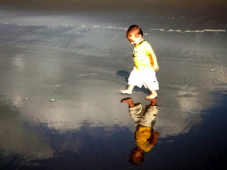 Boy walking on the Beach looking at his reflection