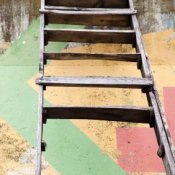 Old wooden ladder leaning against a concrete wall with painted designs.