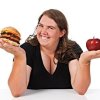 Woman choosing between an apple and a hamburger.
