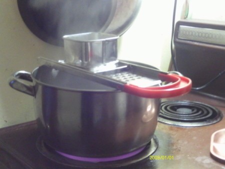 Spaetzle maker on top of a pot of steaming water.