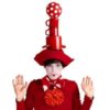 A clown dressed in red balancing cups on their head.