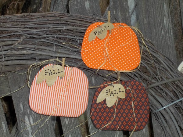 Three pumpkins against a branch wreath and weather wooden fence.