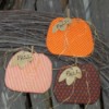 Three pumpkins against a branch wreath and weather wooden fence.