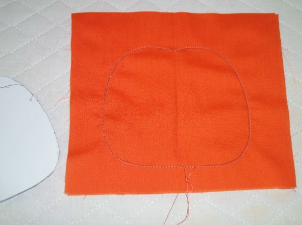 Outline of pumpkin sewn into square orange fabric.