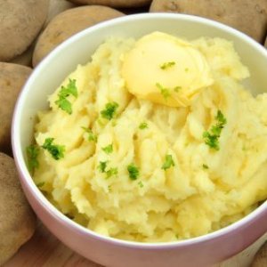 Bowl of mashed potatoes with potatoes in background.