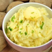 Bowl of mashed potatoes with potatoes in background.