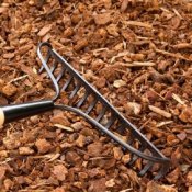 A rake laying on garden mulch.