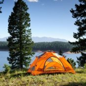 Orange camping tent pitched near a mountain lake.