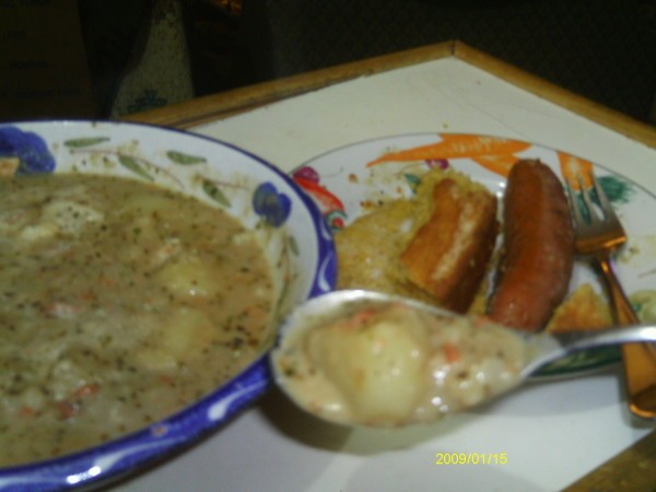 Bowl of the soup, some on spoon, and sausage on the side.