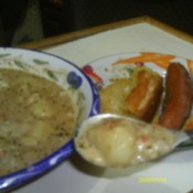 Bowl of the soup, some on spoon, and sausage on the side.