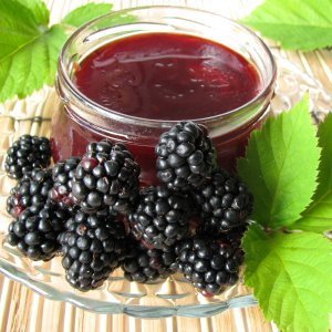 Open jar of blackberry jam with fresh berries on a plate.