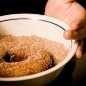 A homemade doughnut being coated in sugar.