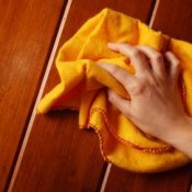 A hand holding a bright yellow cloth to polish a wood surface.
