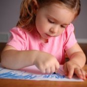 Little girl coloring with a blue crayon on a piece of paper.