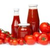 Fresh tomatoes surrounding three bottles of homemade ketchup.